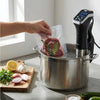 Hand placing a vacuum-sealed package of meat into a pot with a Preservide sous vide smartpro cooker