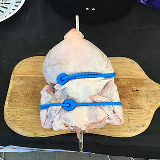 Raw chicken tied with blue blue silicone butcher ties on a wooden cutting board.